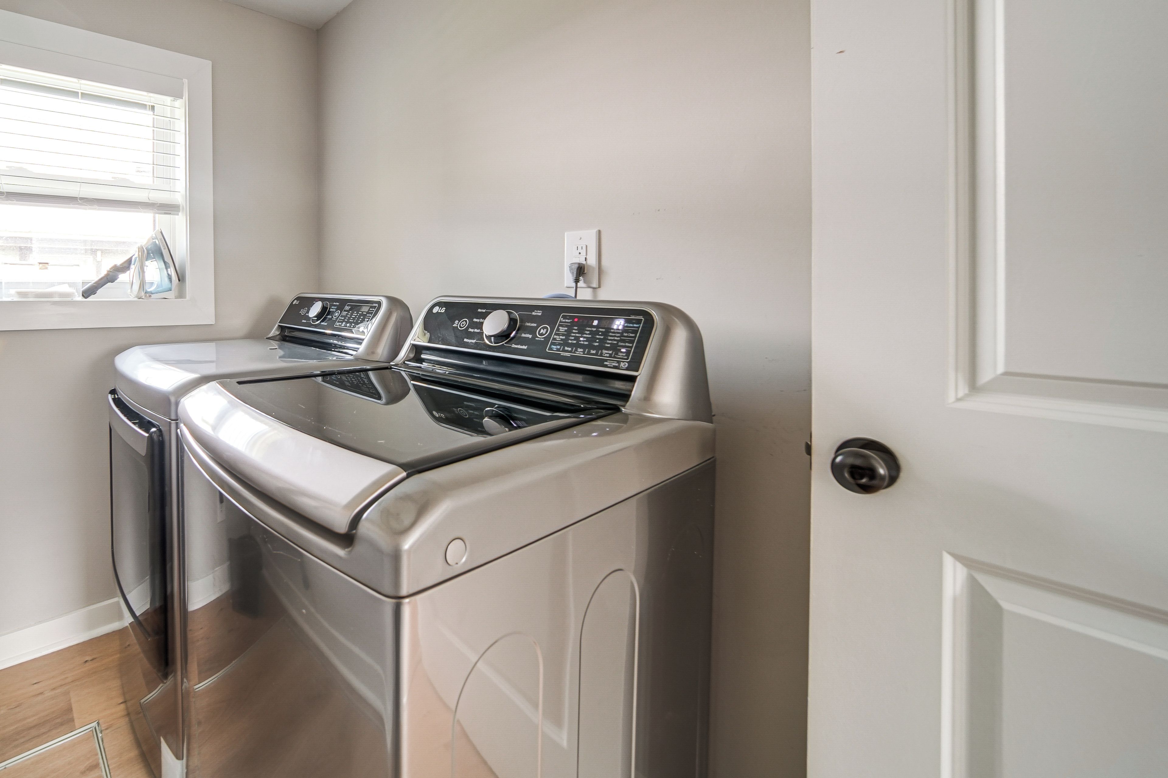 A laundry room with two front-loading washers and dryers, a window with blinds, and a door.