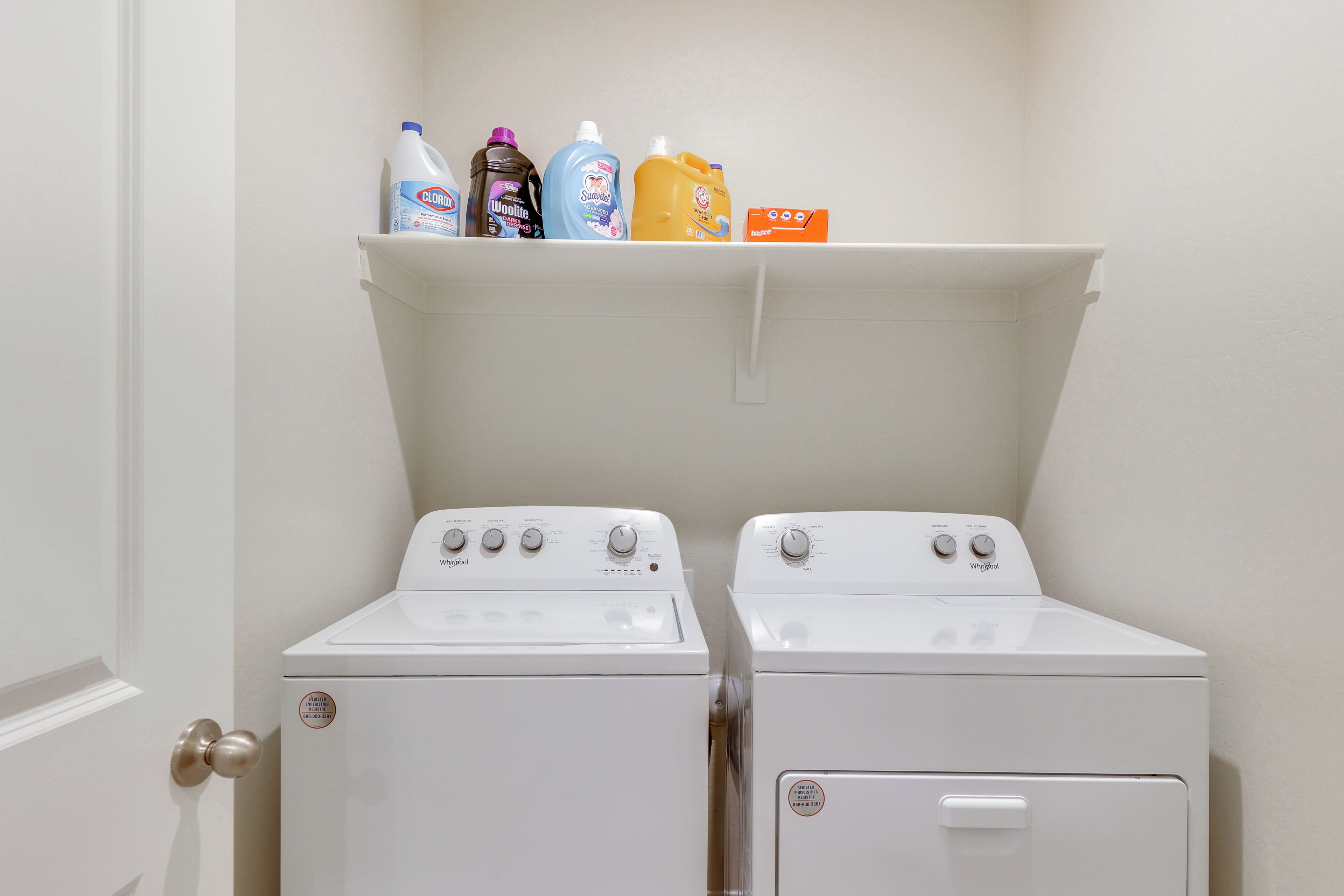 Een wasserette met twee witte Whirlpool wasmachines en een plank daarboven met diverse flessen wasmiddel.