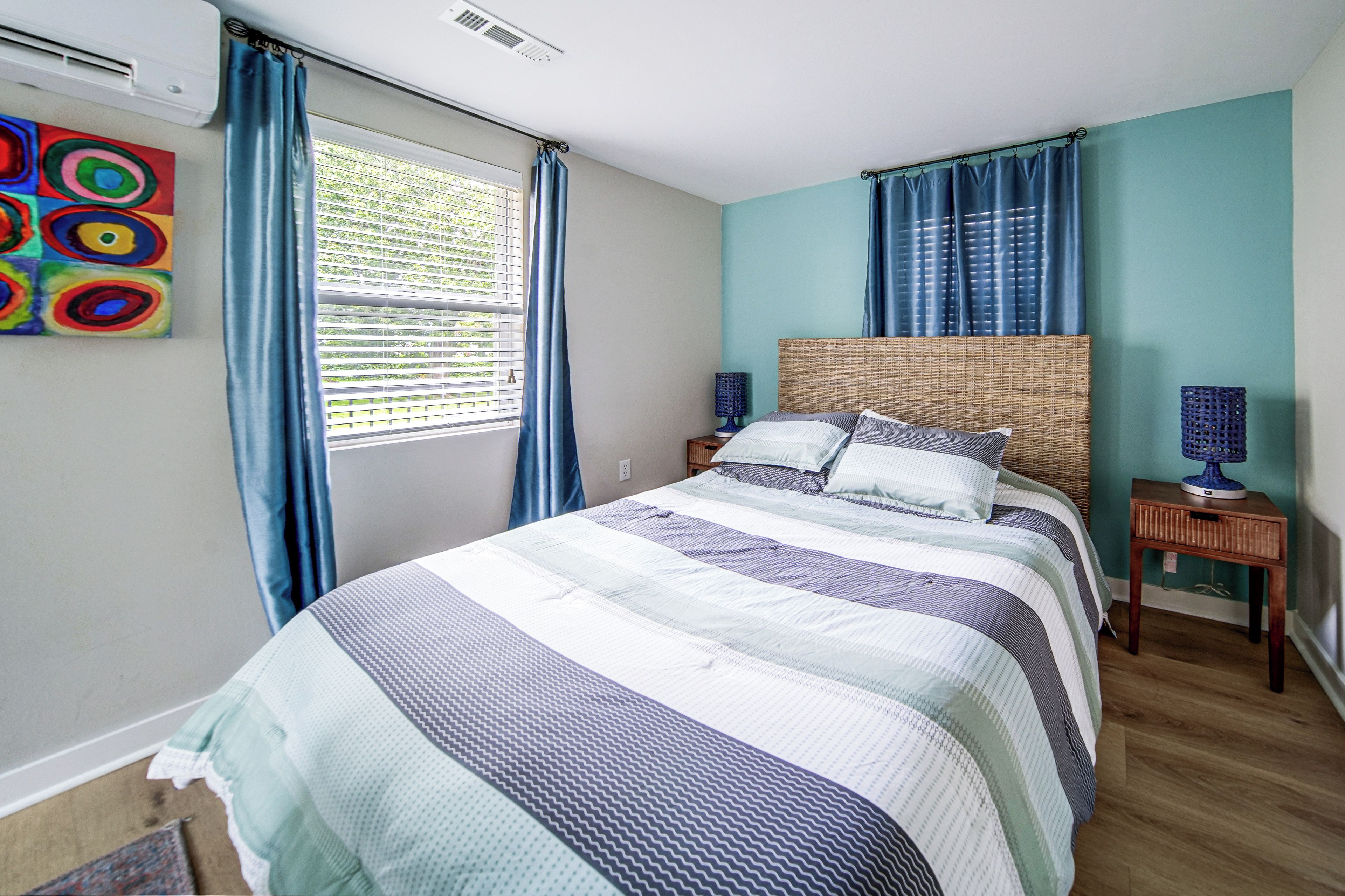 A bedroom with a bed, a nightstand, a lamp, and a window with curtains.