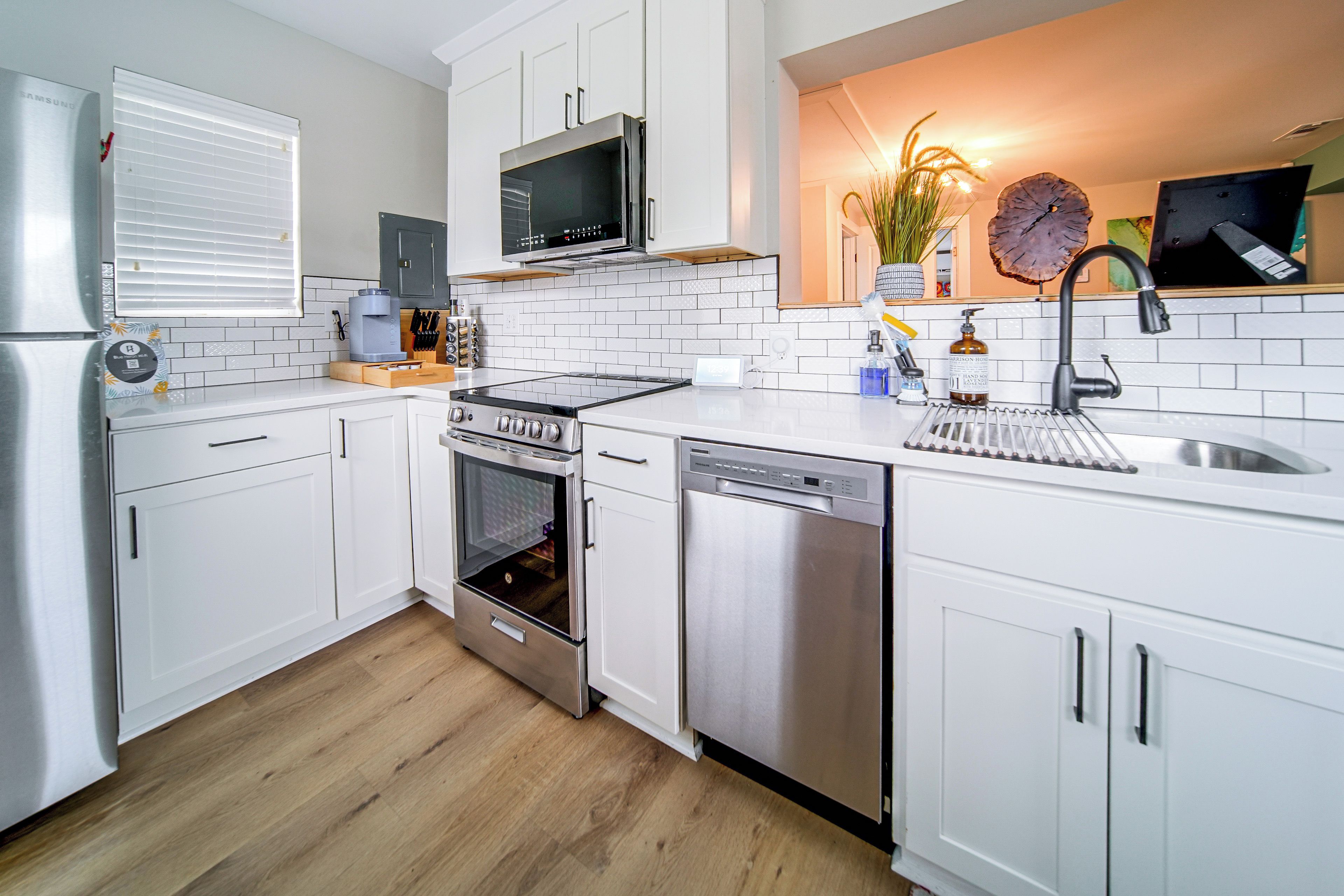 A modern kitchen with white cabinets, stainless steel appliances, and a wooden floor.