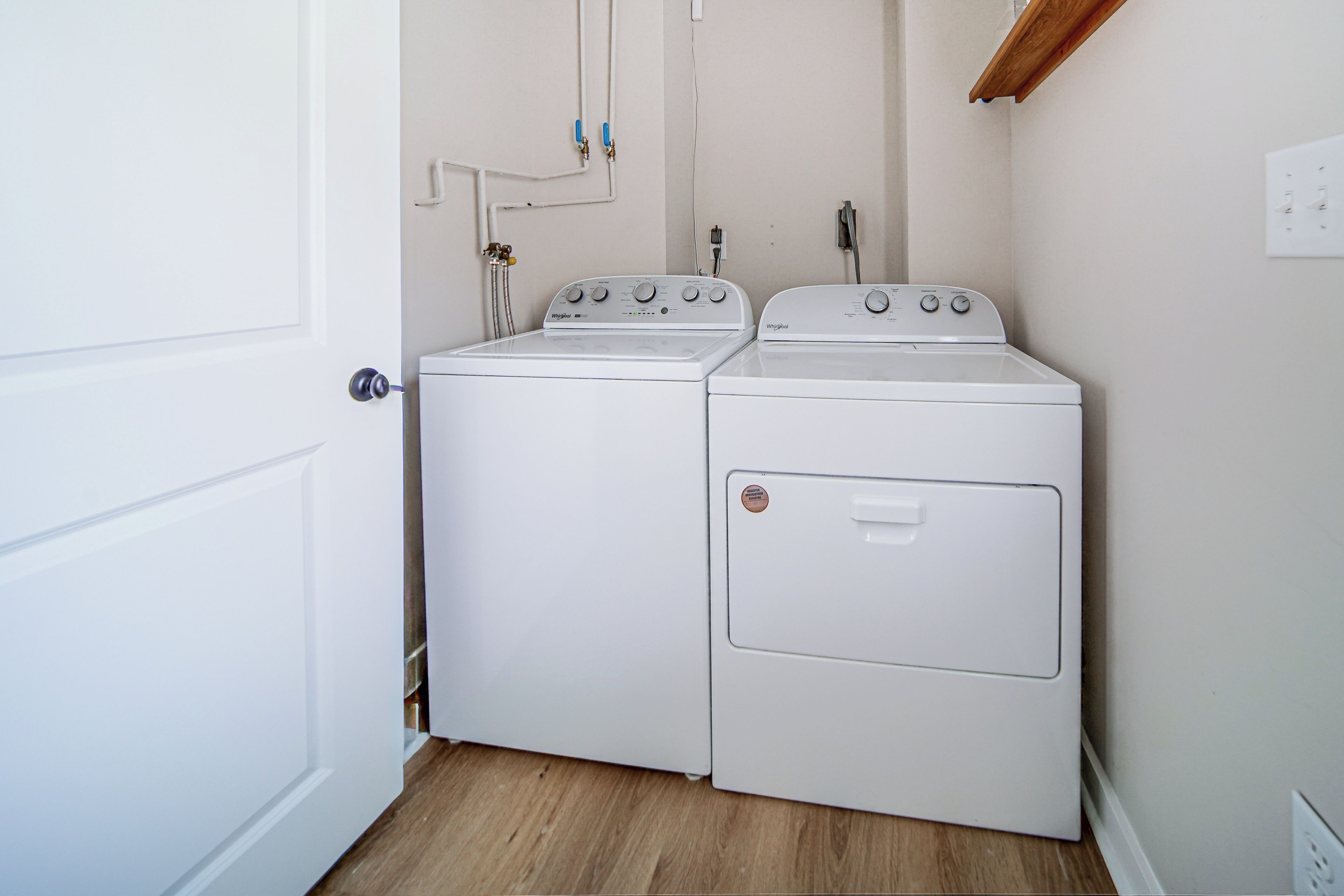A laundry room with two white Whirlpool washers and dryers, a wooden floor, and a white door.