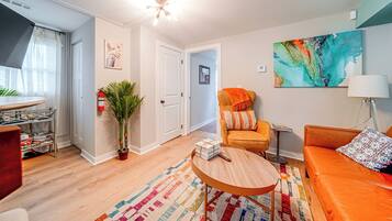 A modern living room with a sofa, armchair, and a coffee table. There is a plant, a fire extinguisher, and a painting on the wall.