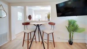 A modern living room with a round table, two chairs, a large mirror, a potted plant, and a flat-screen TV mounted on the wall. - 'Blue Heron' Walk to Kelso Beach! Pet-Friendly Gem (Erie)