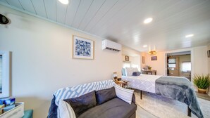 A cozy room with a dark sofa, a bed with a patterned bedspread, a small table with a lamp, and a framed artwork on the wall. - ‘Choo Choo Blue,’ Converted Railcar in DuBois! (DuBois)
