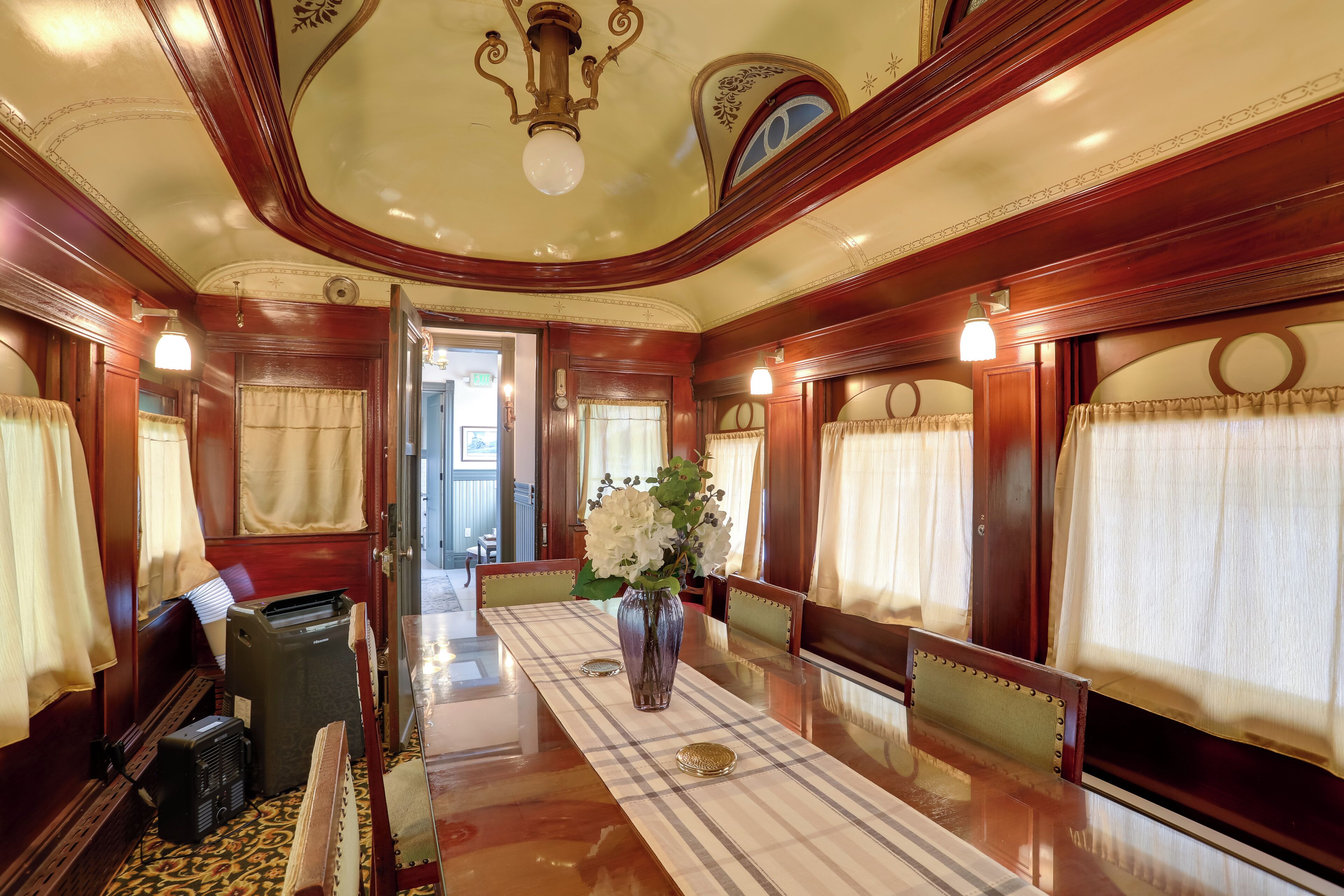 A dining car with a long table, chairs, and a vase with flowers.