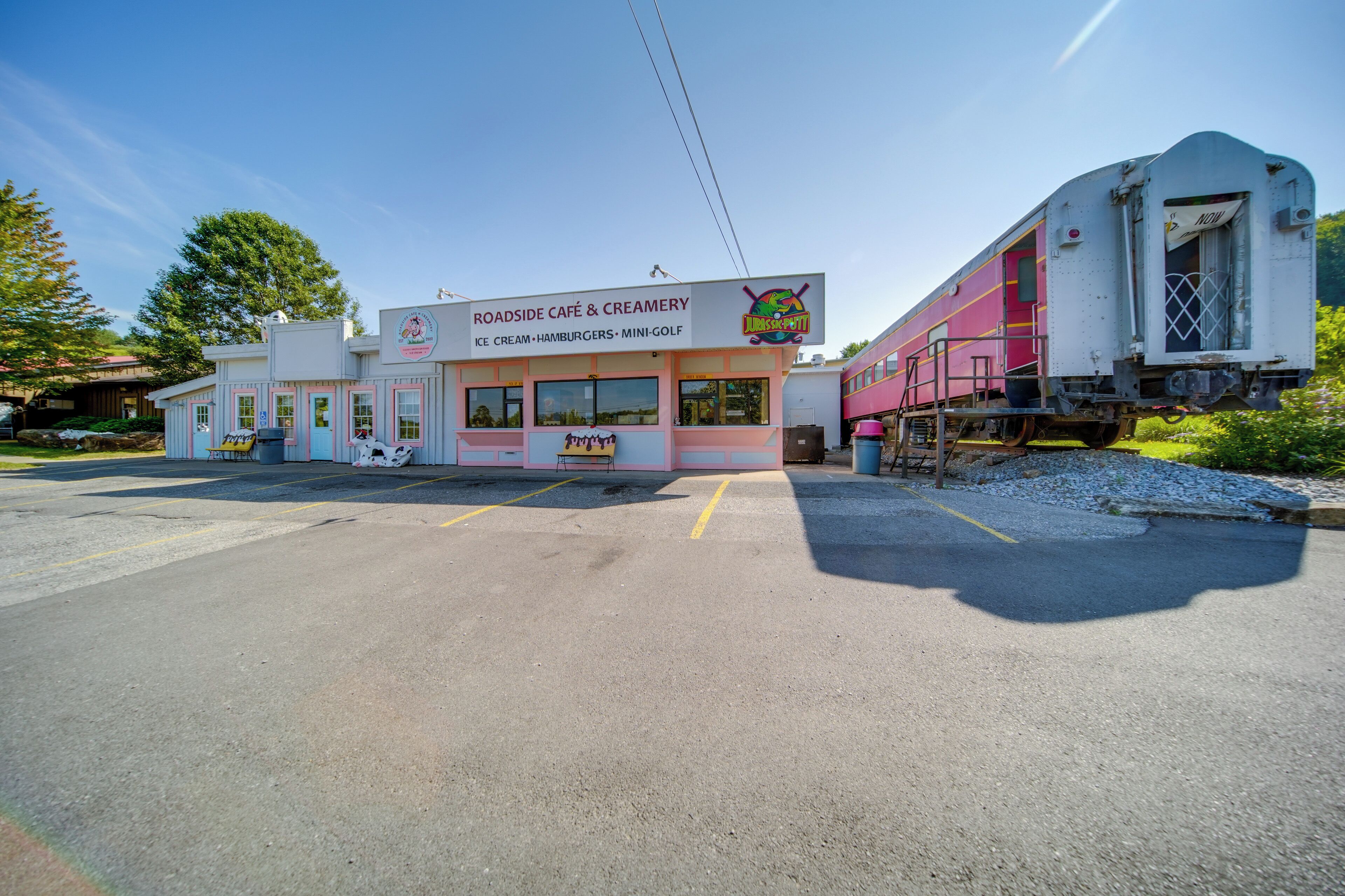 A building with a sign for a roadside café and creamery, a parked train, and a parking lot.