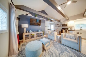 A modern living room with a flat-screen TV, a wooden console, and a seating area with ottomans. - 'Wishin & Fishin' Walkable Erie Home By the Beach! (Erie)
