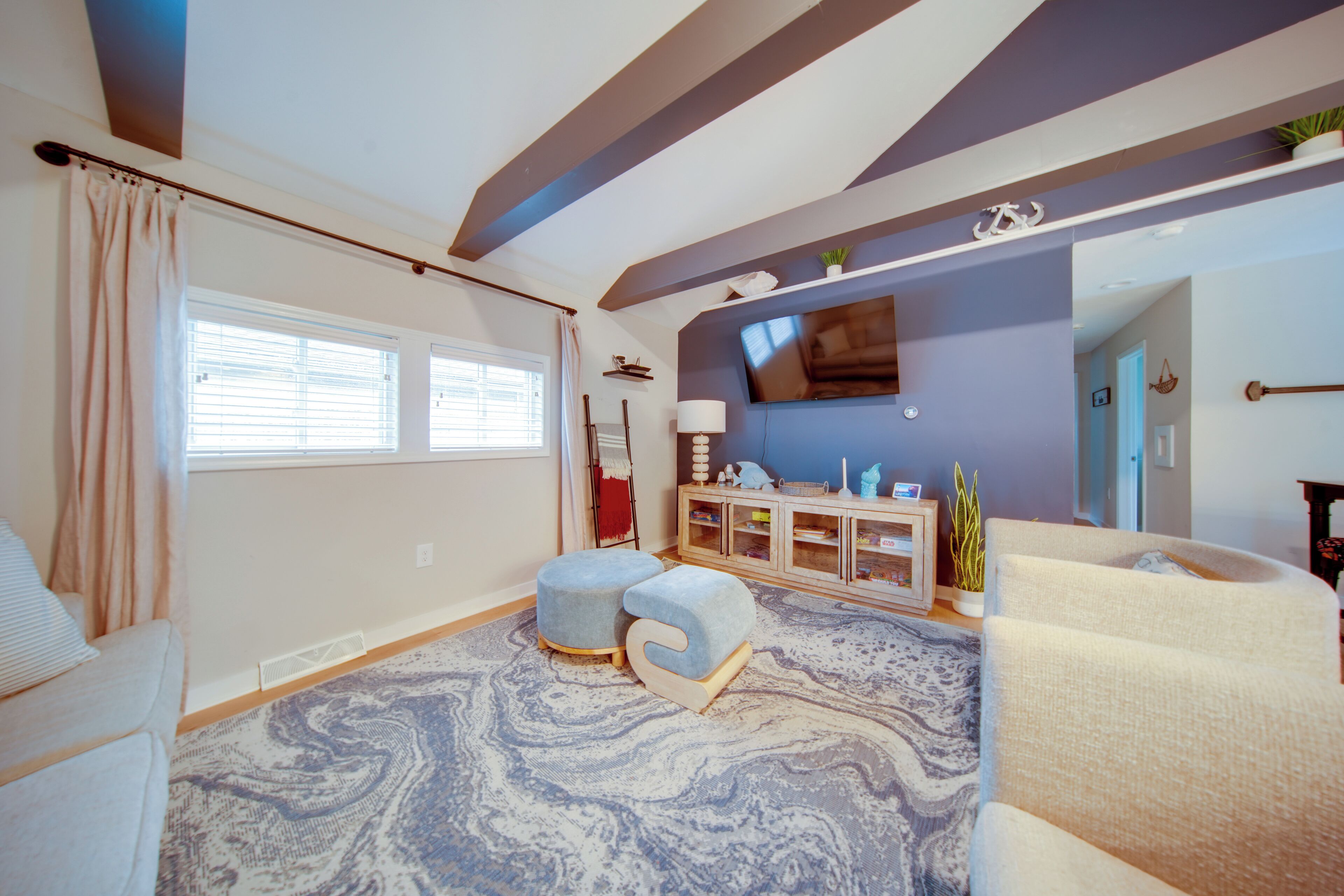 A living room with a large window, a flat-screen TV mounted on the wall, and a patterned rug.