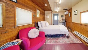 A room with wooden paneling, a bed with white bedding, a red armchair, and a patterned rug. - 'Red NY Central,' Converted Railcar in DuBois! (DuBois)
