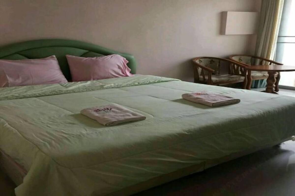 A neatly made bed with pillows, a chair, and a lamp in a room with a window.