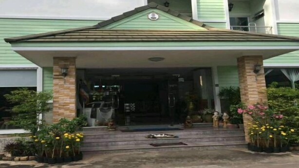 A building with a green facade, a covered entrance, and a small garden area with potted plants and flowers. - Wanpen Place (Udon Thani)