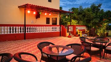 Une terrasse extérieure avec des murs rouges et blancs, une pergola décorée de guirlandes lumineuses et du mobilier d’extérieur.