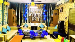 A living room with a sofa set, a coffee table, and a TV. There are balloons and streamers on the walls. - Shreejee The Farm | Huge Farm•Pool•Party•Desi Fun (Sancholi Village)