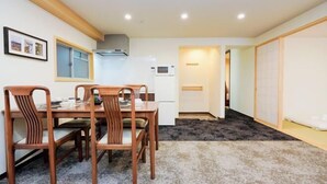 A room with a dining table and chairs, a kitchen area with a stove and microwave, and a sliding door leading to another room. - Asobo osaka nipponbashi Apartment (Osaka)