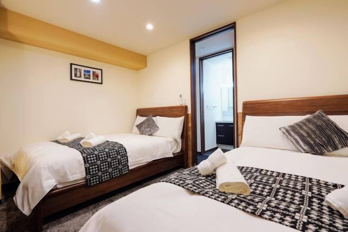 Une chambre d’hôtel avec deux lits, une tête de lit en bois, un tableau encadré au mur et une porte donnant sur une salle de bain.