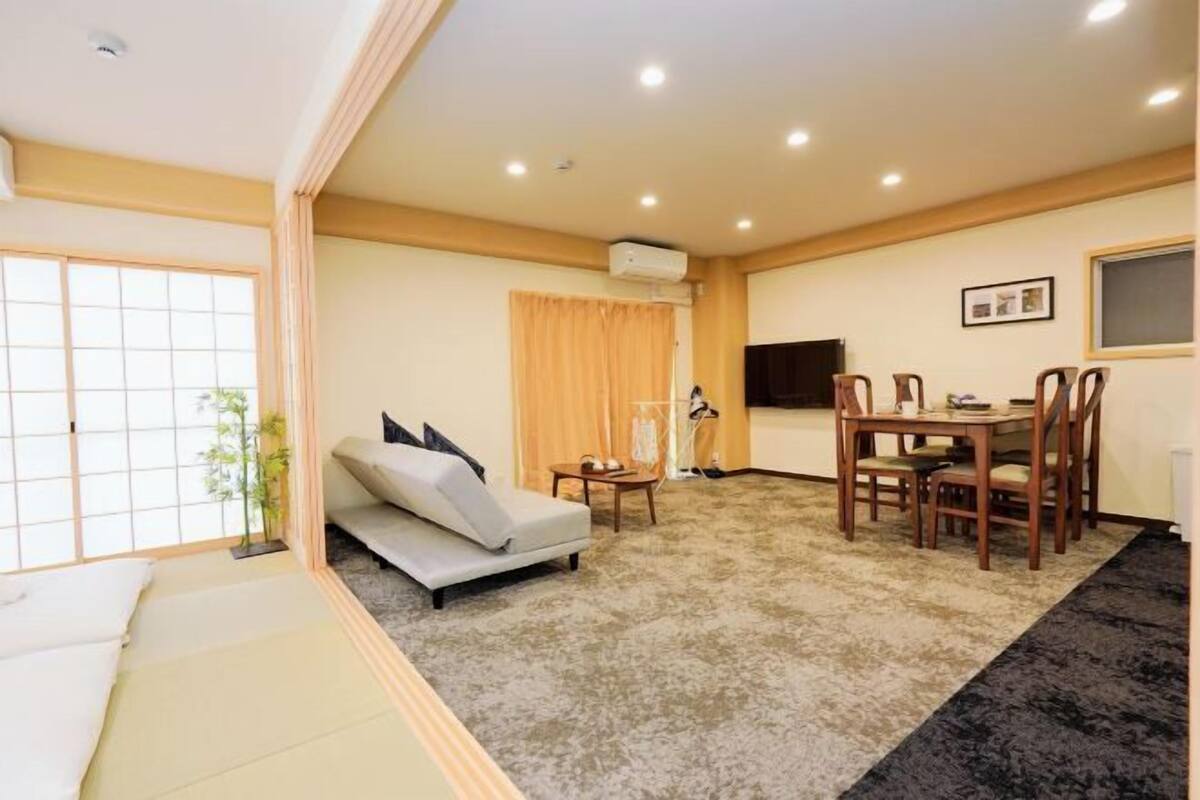A room with a sofa, a dining table with chairs, a TV, and a window with curtains.
