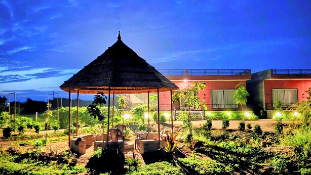 A gazebo with a thatched roof surrounded by greenery and a building with red walls and a balcony. - Gokul Jawai (Bali)