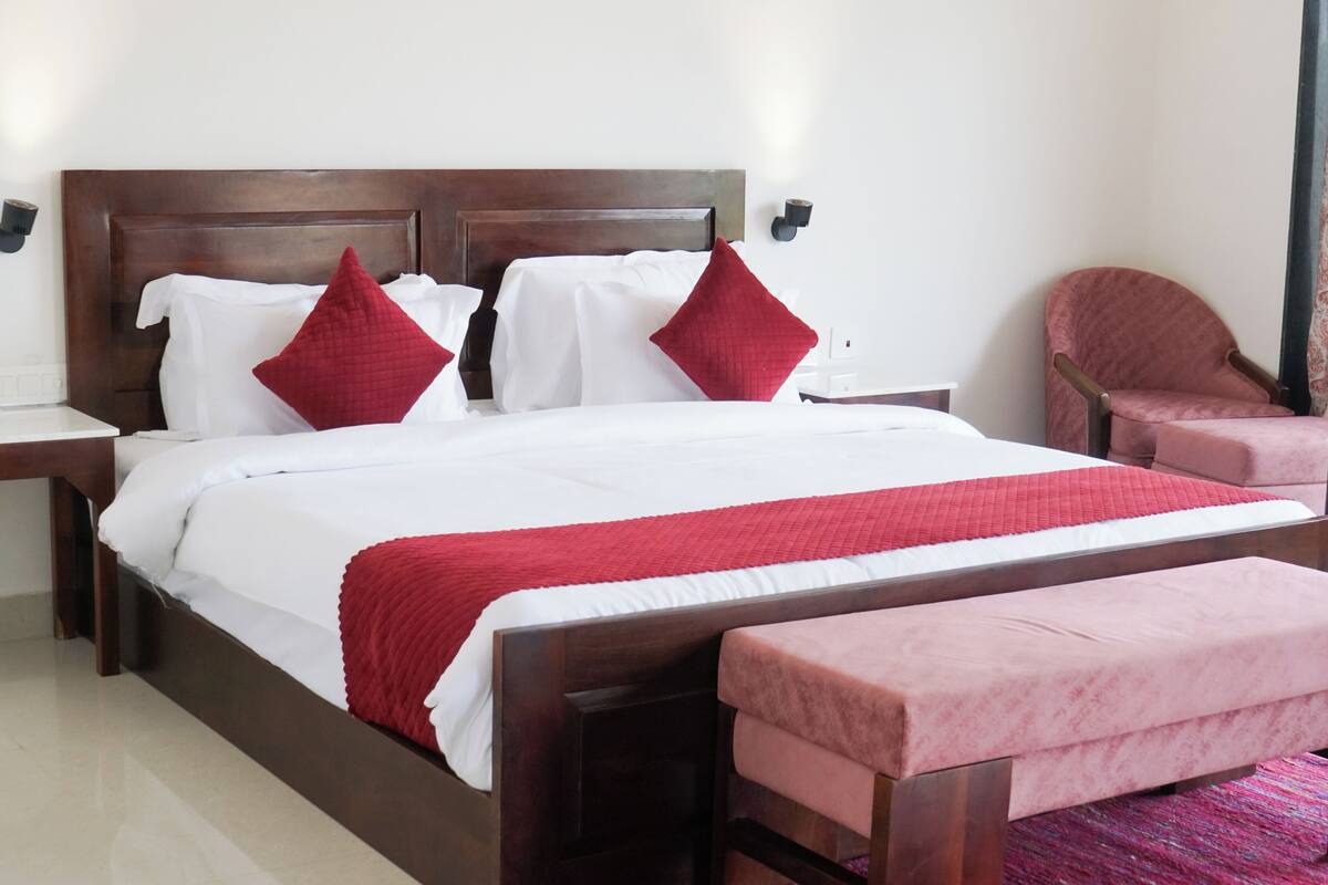 A hotel room with a large bed, two bedside tables, a wooden headboard, and a pink armchair.