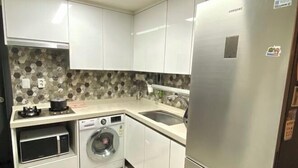 A compact kitchen with white cabinets, a stainless steel refrigerator, a washing machine, and a microwave. - RED PANDA COMMERCE (Seoul)