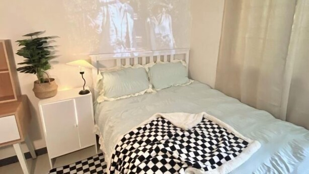 A bedroom with a bed, a nightstand, a lamp, a potted plant, and a projection on the wall. - RED PANDA COMMERCE (Seoul)