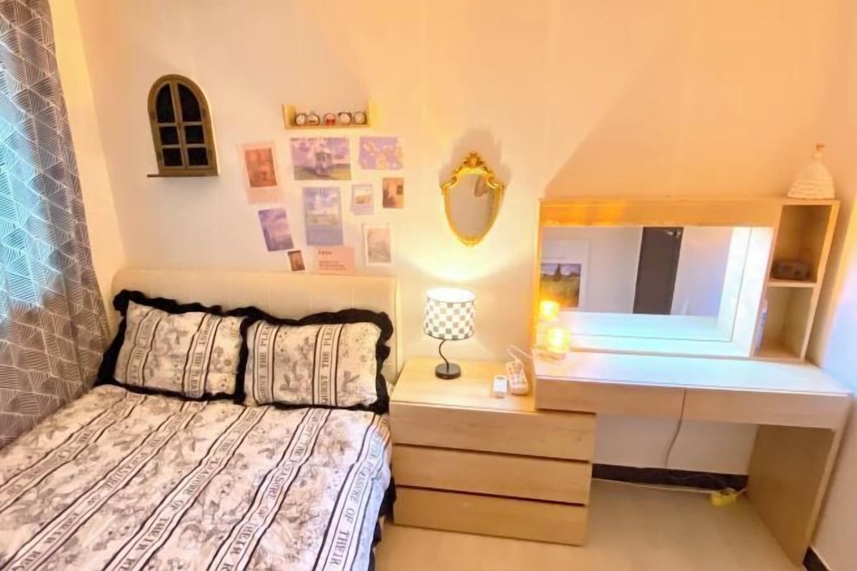 A bedroom with a bed, bedside table, lamp, mirror, and wall decorations.