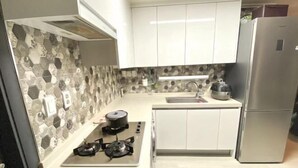 A modern kitchen with white cabinets, a gas stove, a sink, and a stainless steel refrigerator. - RED PANDA COMMERCE (Seoul)