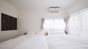 Quarto de hotel com duas camas, uma mesa de cabeceira com abajur, ar condicionado e janela com cortinas.