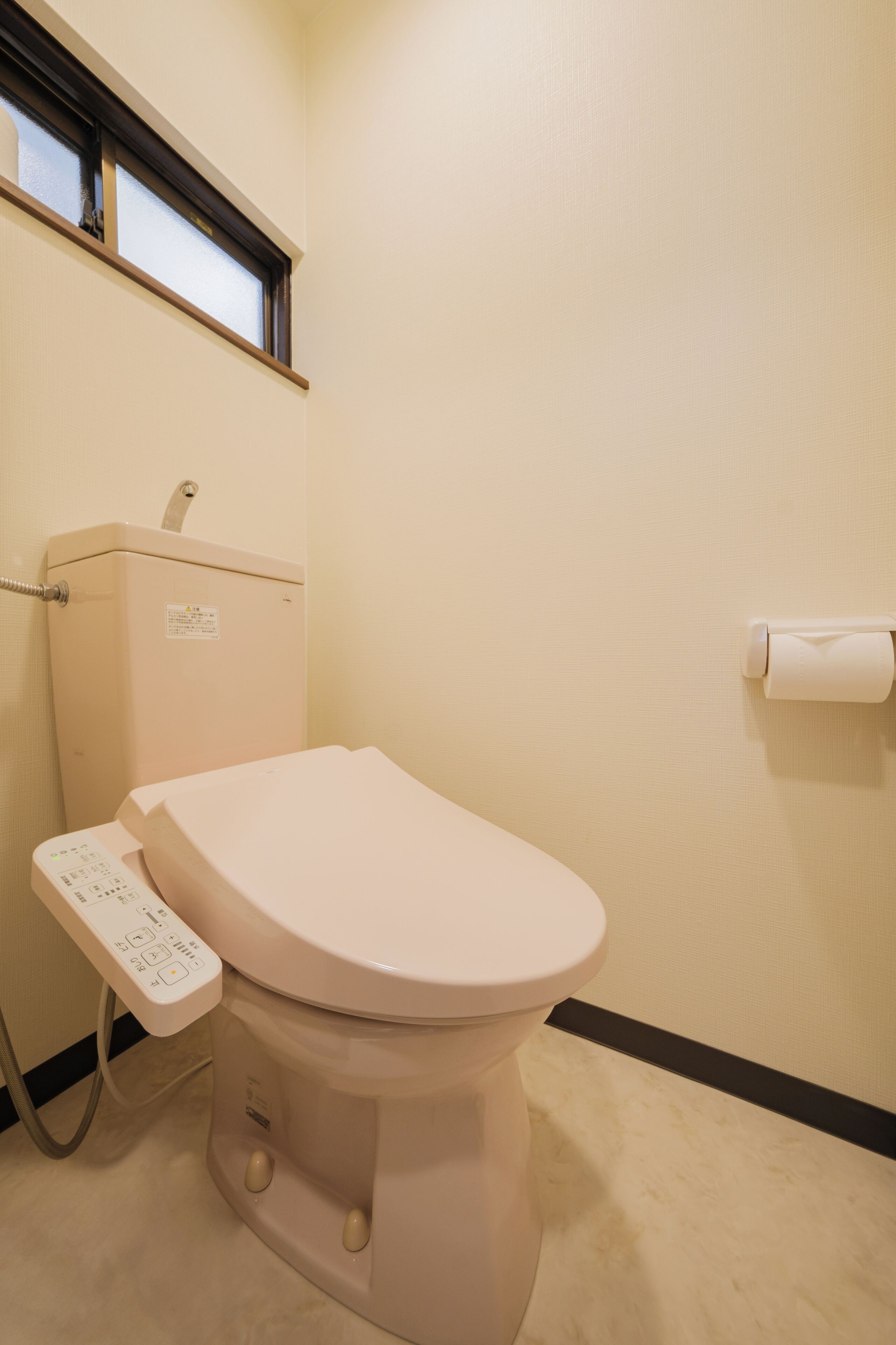 Inodoro con panel de control, soporte para papel higiénico y una ventana sobre el inodoro.