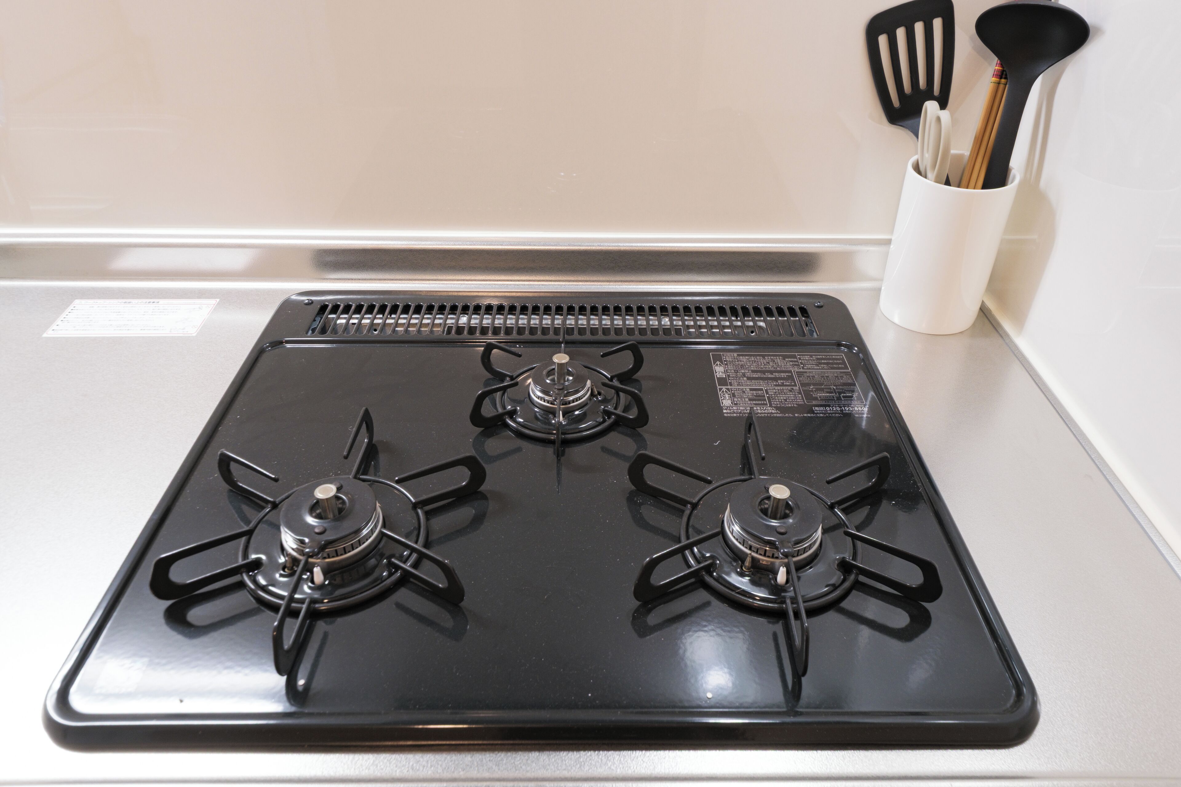 Una cocina con estufa negra, pared blanca y un organizador de utensilios con espátulas y cuchara.