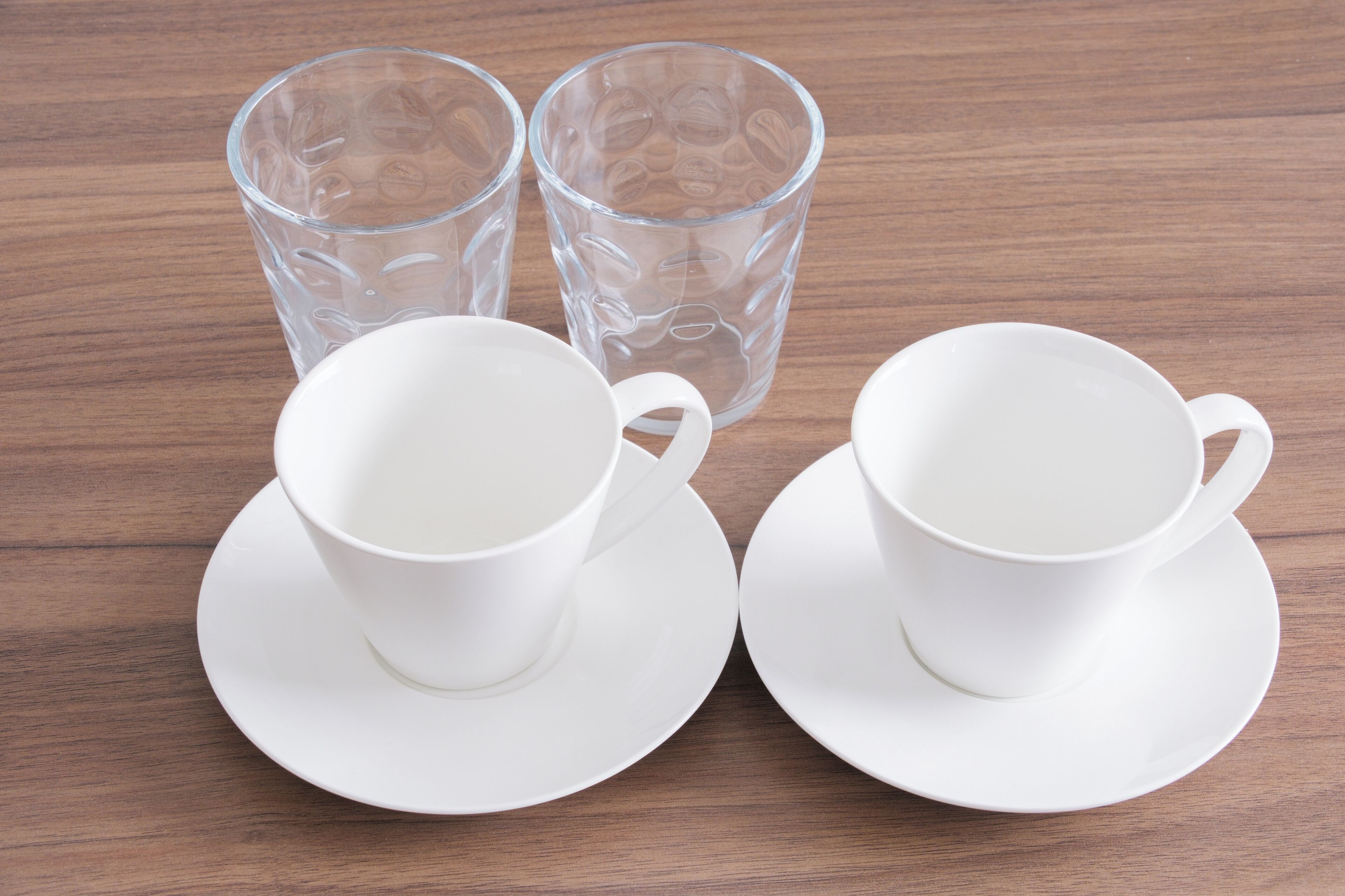 Two white cups and saucers on a wooden table.