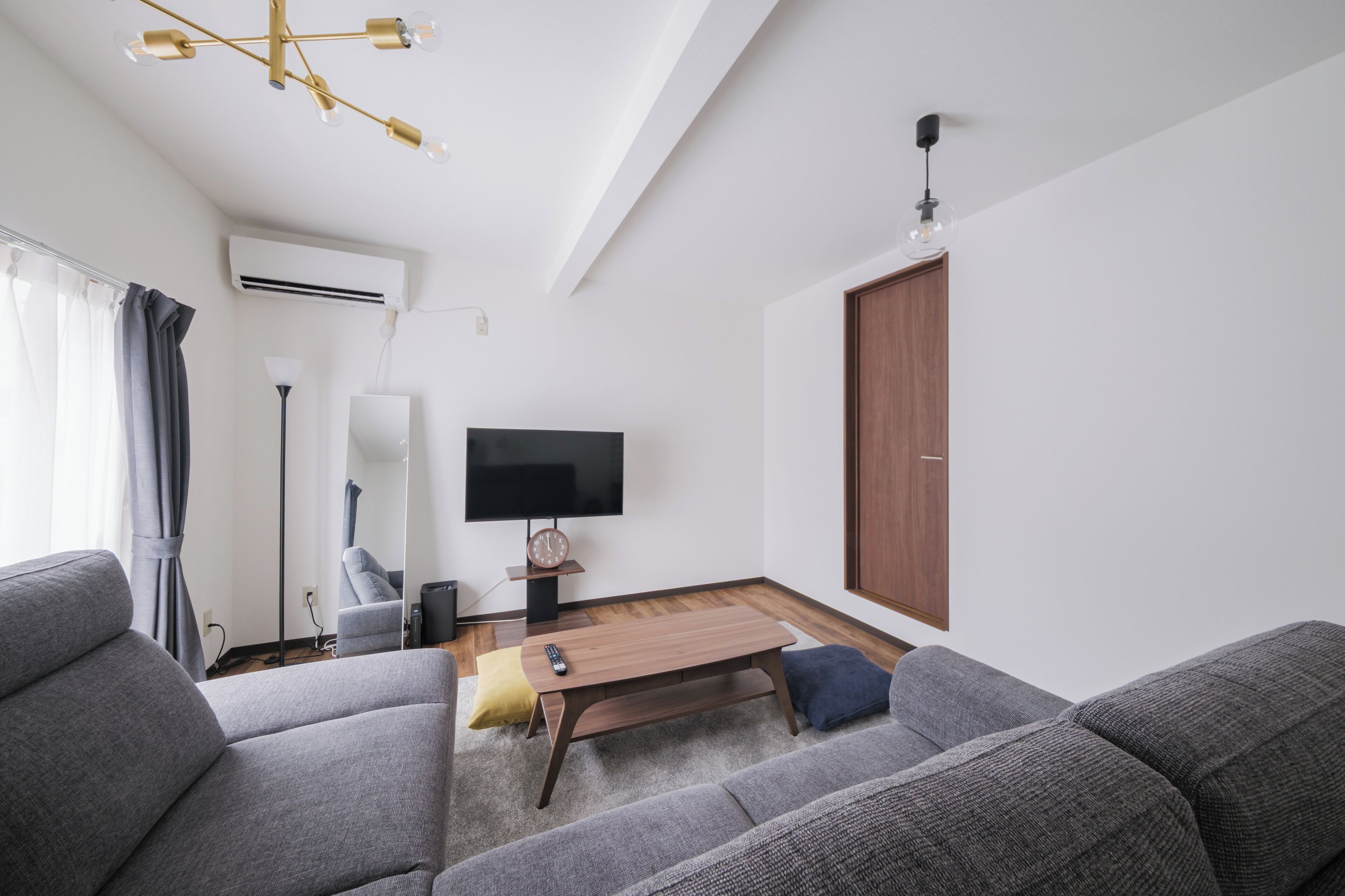 A modern living room with a flat-screen TV, grey sofas, a wooden coffee table, and a ceiling light fixture.