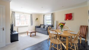 A living room with a sofa, dining table, chairs, a TV, and a window with curtains.