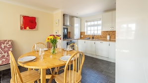 A dining area with a wooden table set for four, a kitchen with white cabinets, and a red abstract painting on the wall.
