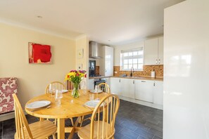 A dining area with a wooden table set for four, a kitchen with white cabinets, and a red abstract painting on the wall. - Arundel Central Apartment with rare parking. Pet Friendly. (Arundel)