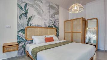 Une chambre avec un grand lit, une tête de lit en rotin, une armoire en osier, un miroir et un luminaire au plafond.