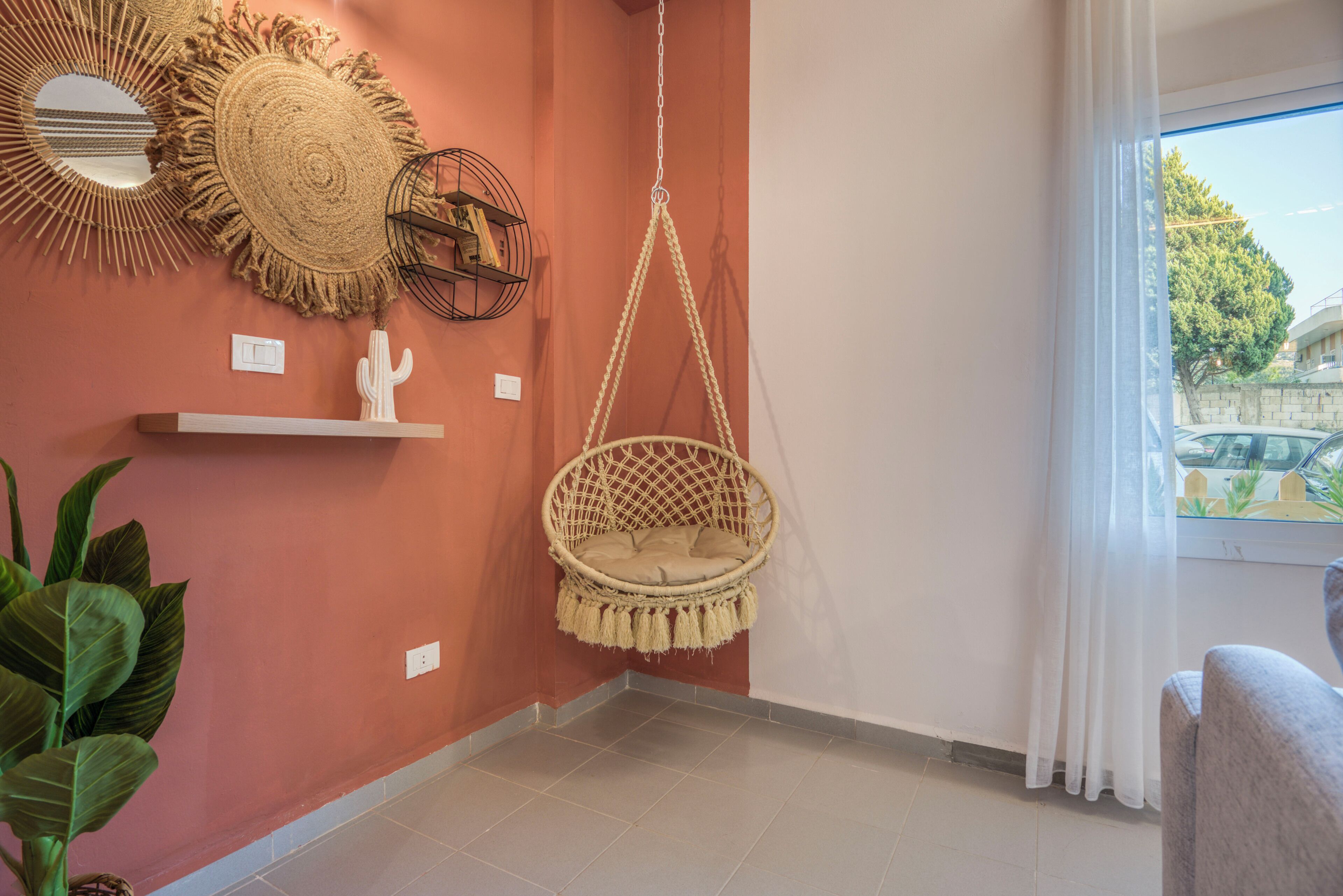 Une pièce avec un fauteuil suspendu, un miroir rond et une étagère sur laquelle se trouve un cactus.