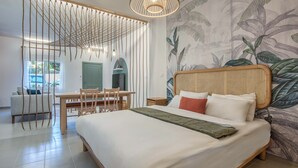 A bedroom with a bed, a dining table, chairs, a hanging light fixture, and a wall with a tropical leaf pattern. - Natura Studio & Balcony in Batroun (Batroun)