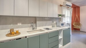 Et moderne køkken med en hvid bordplade, en indbygget vask og en mikrobølgeovn. Der er en hængestol og en lille plante på bordet.
