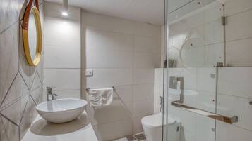 A modern bathroom with a large vessel sink, a glass shower enclosure, and a toilet.