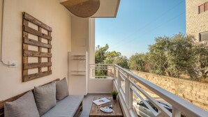 En balkon med træbænk, et lille bord med tegnegrej, samt udsigt til en bil og træer.