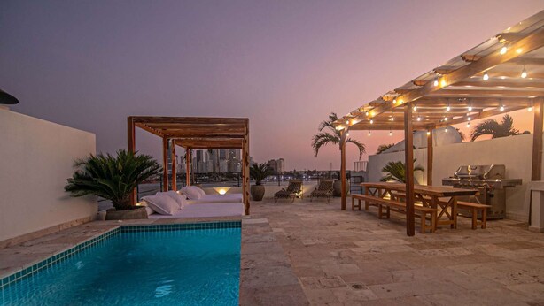 Un espace piscine aménagé sur le toit, avec une pergola, des chaises longues et un barbecue.