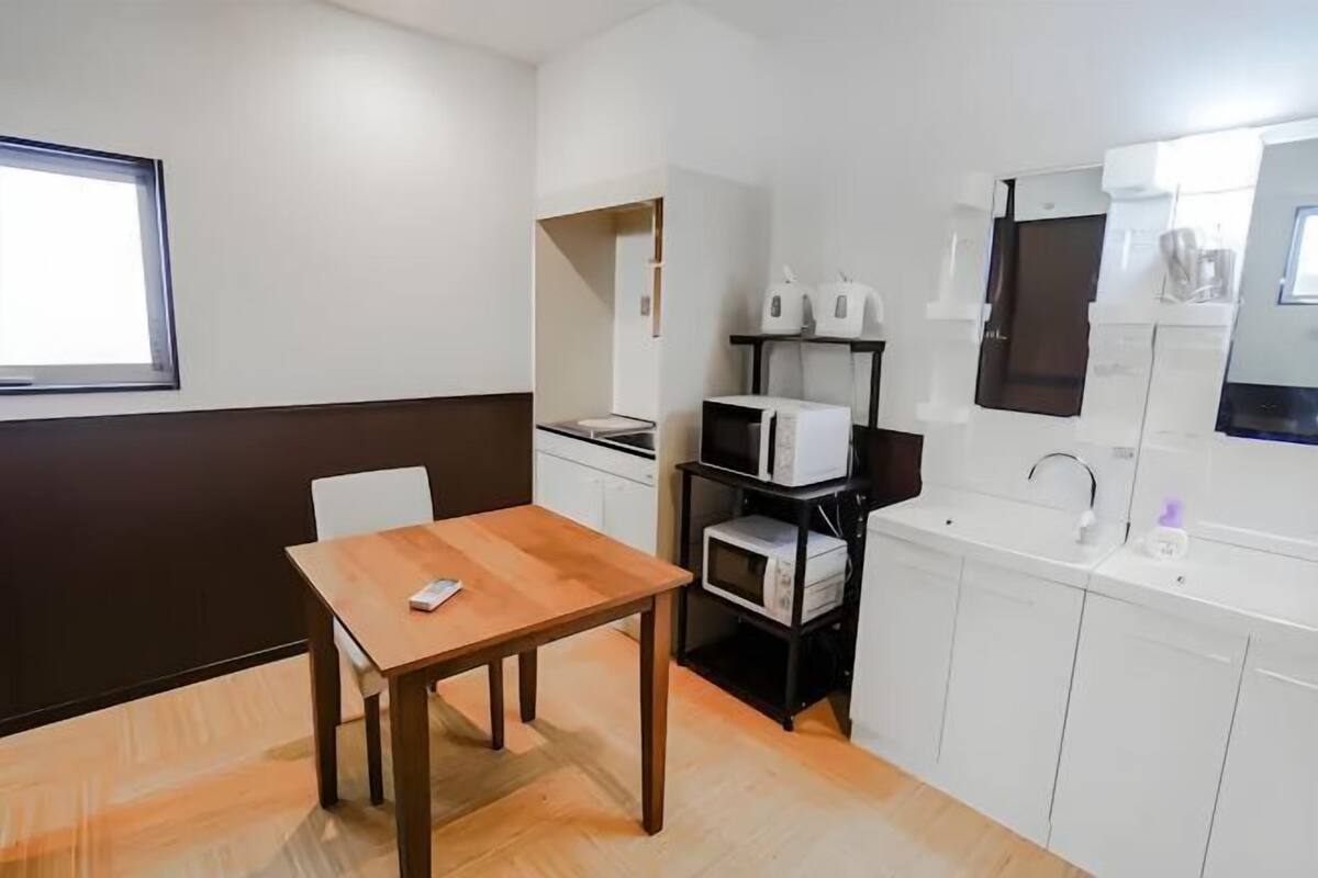 A compact kitchen with a wooden table, white cabinets, a microwave, and a coffee machine.