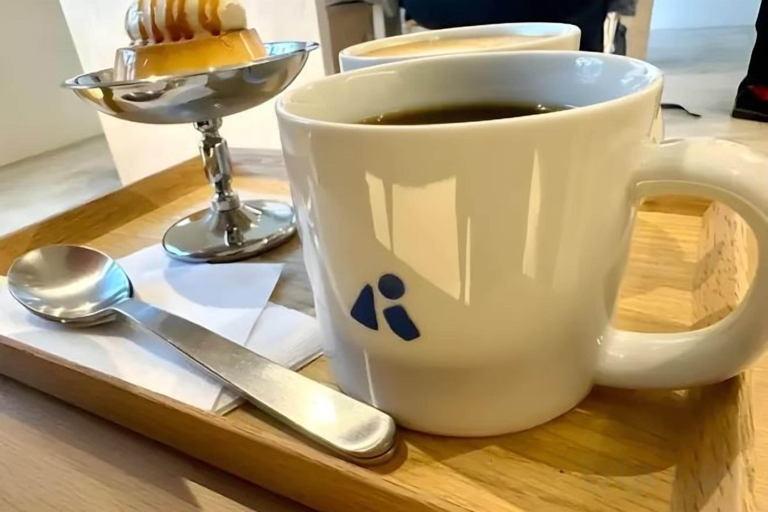 Une tasse blanche ornée d’un motif bleu, une cuillère et une petite assiette contenant un dessert, le tout posé sur un plateau en bois.