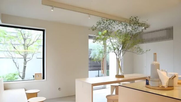 Une pièce moderne et minimaliste, dotée d’une grande fenêtre, d’un bureau en bois et d’un petit coin salon.