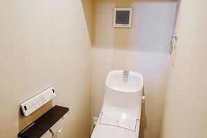 A small, compact bathroom with a white toilet, a wall-mounted air vent, and a power outlet with a control panel. - SAMURAI STAY Senzoku Pond【MALE ONLY】 (Tokyo)