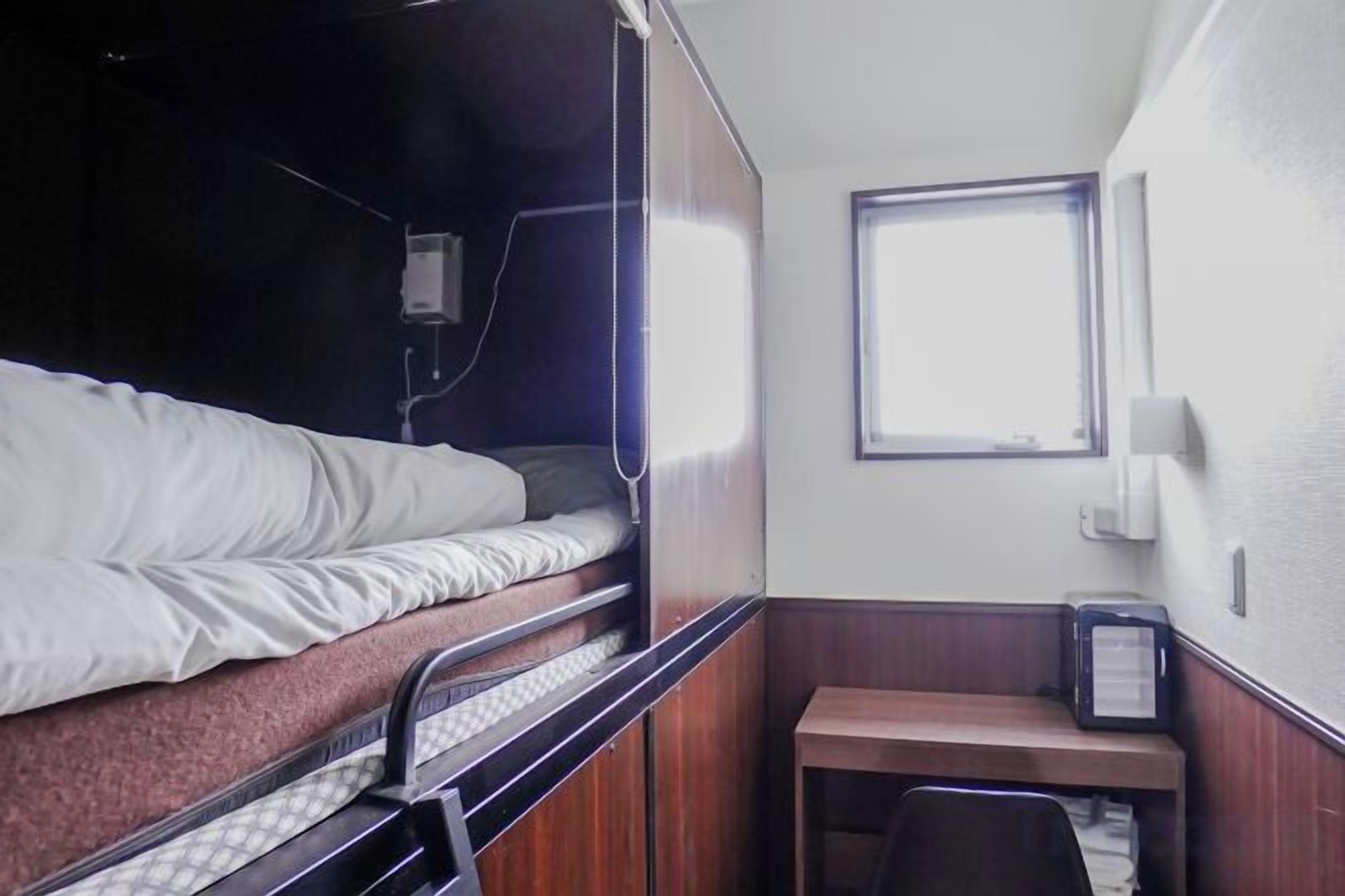 A bunk bed with a window, a desk with a chair, and a small table.