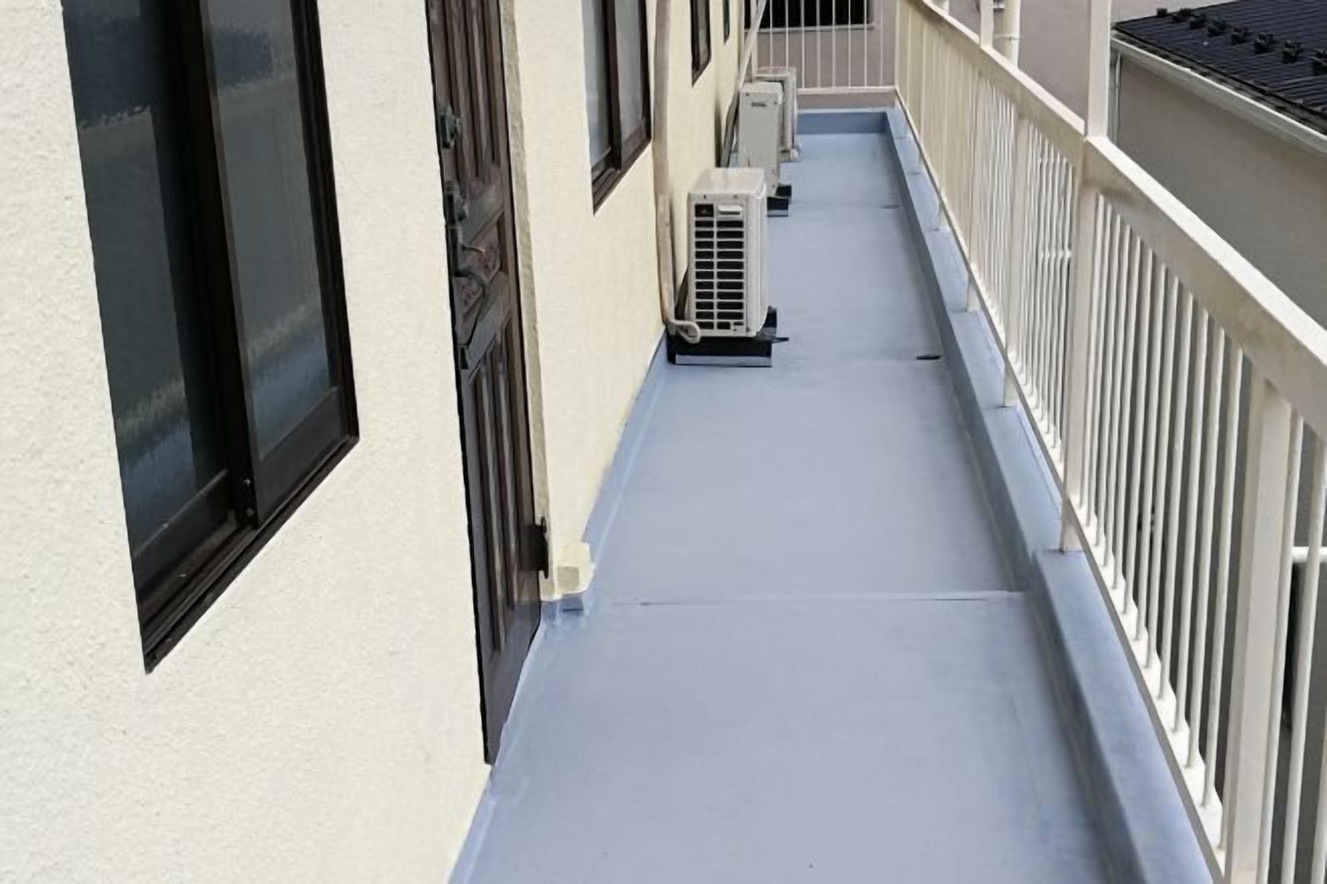 Un corridoio stretto con condizionatori a destra, una ringhiera bianca a sinistra e un tetto piatto.