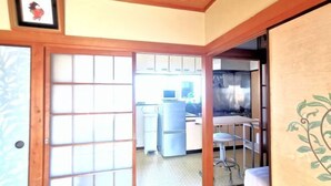 A traditional Japanese room with tatami flooring, a sliding door, and a kitchen area visible through the door. - Tokyo Yoshimi home stay (Tokyo)