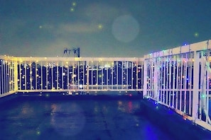 A rooftop terrace with a glass railing, a metal railing, and a view of the city skyline at night. - Tokyo Yoshimi home stay (Tokyo)