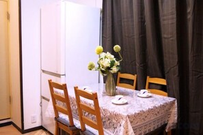 A dining table with a lace tablecloth, two chairs, a vase with flowers, and a white refrigerator in a room with a curtain. - Tokyo Yoshimi home stay (Tokyo)